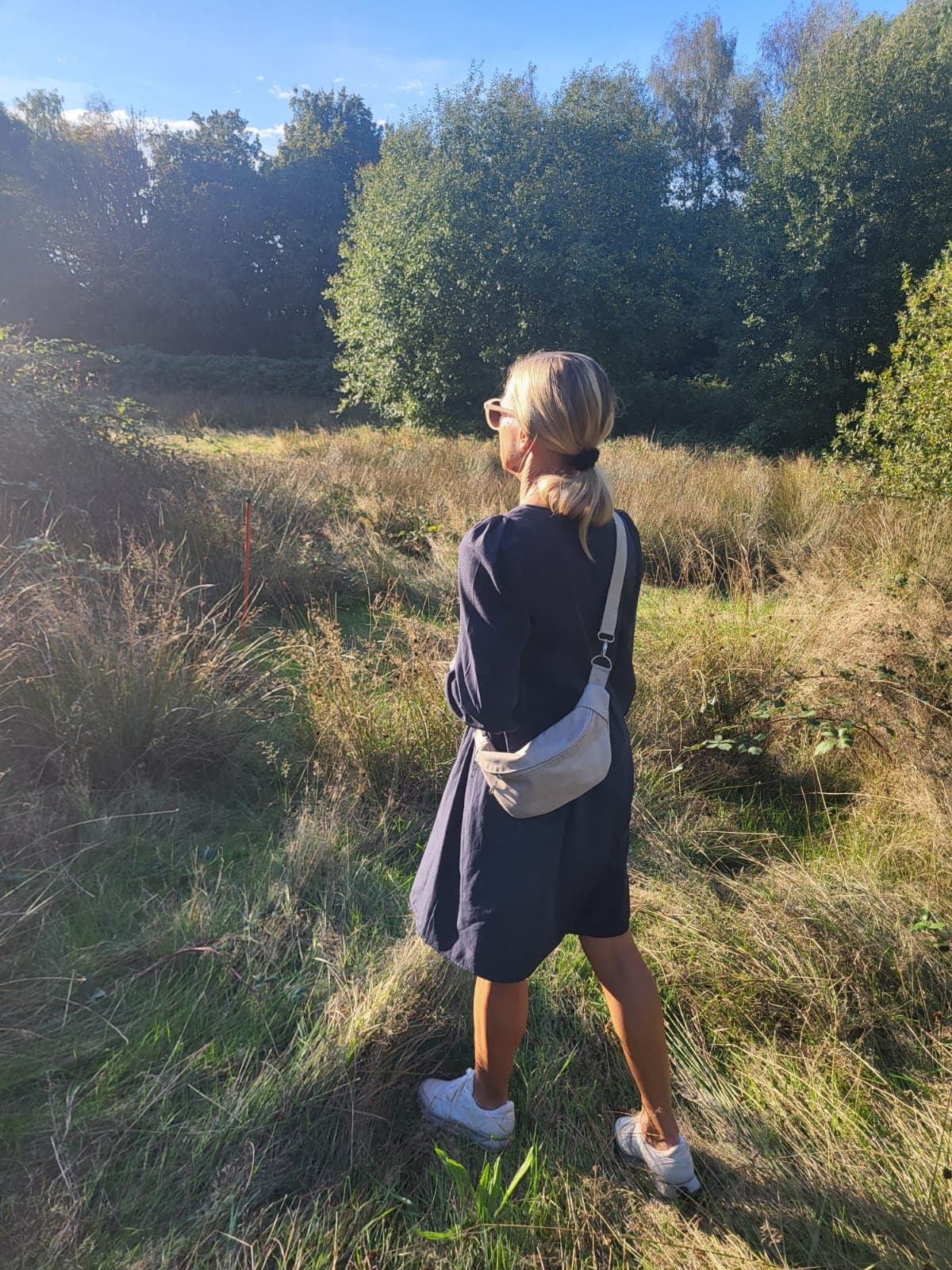 Frau geht durch eine Wiese und trägt die Sling in Hellblau quer über dem Rücken